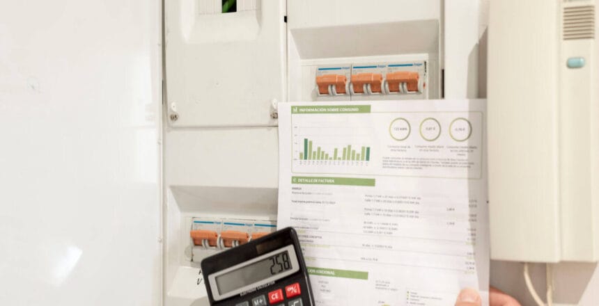 a hand holding an electricity bill and calculator in front of power control switch, concept of electricity price increase