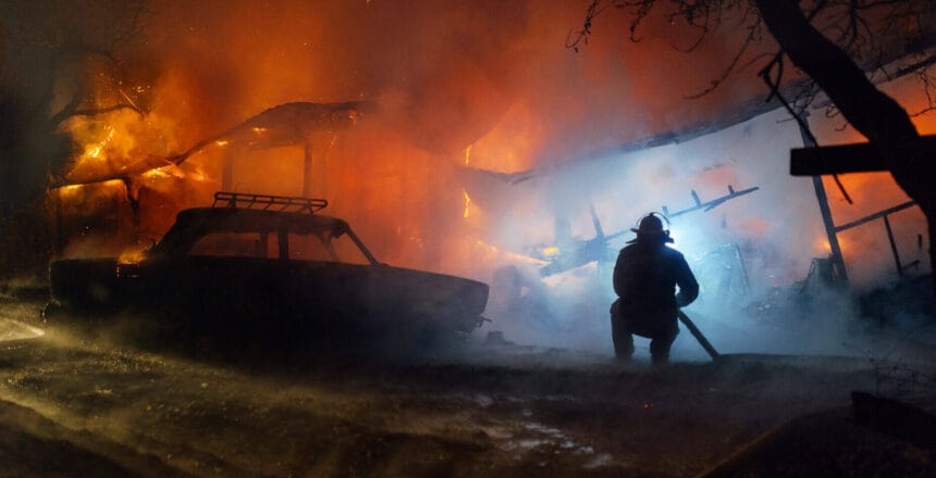 Firefighter putting with the hose out the fire of the house and car at night accident