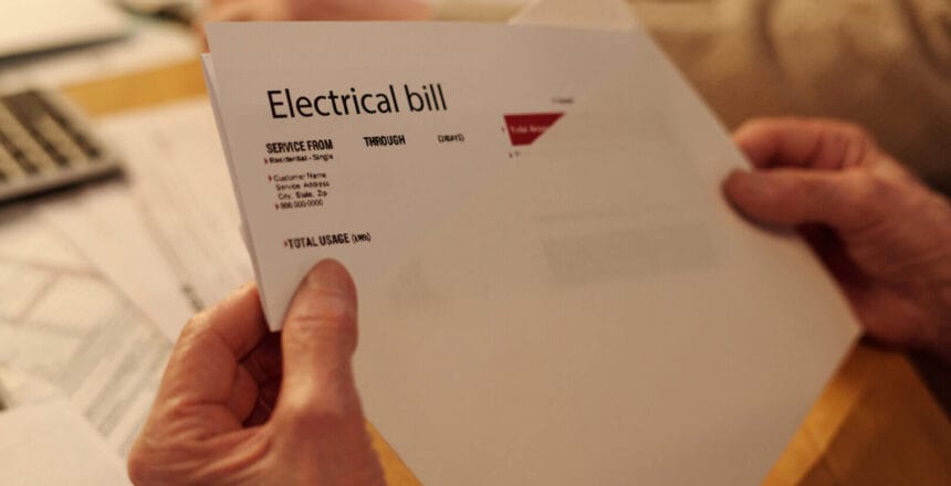 Hand of unrecognizable elderly woman taking folded electrical bill out of white envelope while sitting by table and checking payment documents