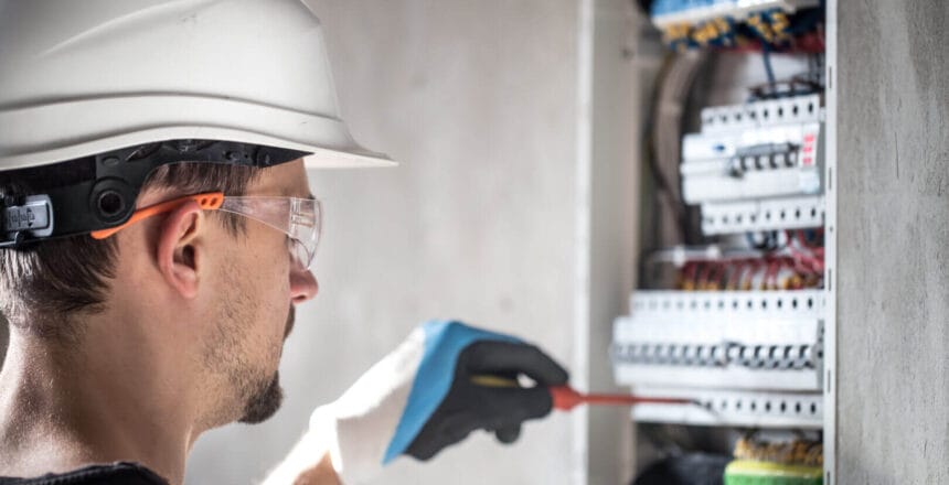 Man, an electrical technician working in a switchboard with fuses. Installation and connection of electrical equipment. Professional with tools in hand. concept of complex work, space for text.